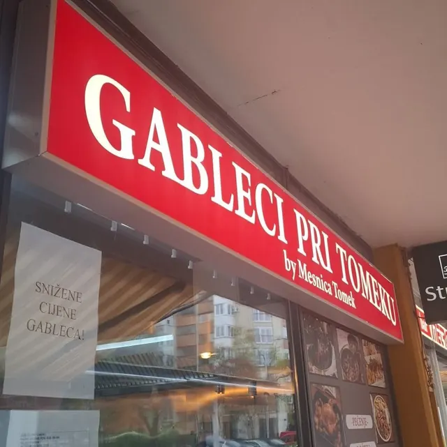 Crveni osvijetljeni natpis „Gableci Pri Tomeku by Mesnica Tomek“ iznad izloga zalogajnice